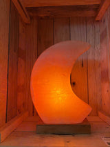 Maanvormige Himalaya zoutlamp in roze, grijs en wit met zachte gloed en houten voet.